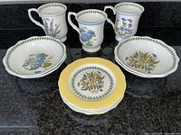 Front view of 3 mugs, 2 fruit/cereal bowls, and 4 dessert plates showing botanical floral designs and yellow rim on plates