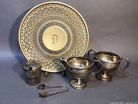 Photo of entire set showing the nickel silver reticulated footed dish with engraved D, weighted sterling creamer and sugar bowl, reticulated jar cover with glass insert, and sugar cube tongs.