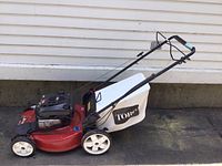 Side profile view of the Toro 22-inch front drive mower with white clipping bag attached and black handlebar, showing red deck and white wheels.