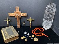 Lot arranged on black cloth background showing waterford holy water font, antique bible, crucifixes, amber prayer beads, and religious pendants and medallions