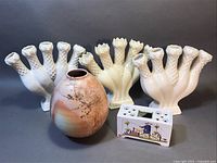 Lot arranged with five vases: three white ceramic posey holders in back row, the hand thrown pottery vase in front center, and a small decorative electronic item also in front for scale.