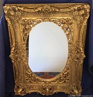 Front view of the large ornate gold leaf mirror with oval opening showing intricate carved frame details.