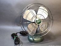 Front angled view showing metal blades, protective cage, and original electrical cord with inline switch beside the fan base.