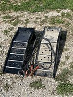 Pair of black metal car ramps placed on grassy gravel surface with booster cables laid on top