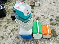 Photo showing stacked and grouped coolers outdoors on gravel. Teal Little Playmate cooler is on top of a green and four other coolers in various colors and sizes.