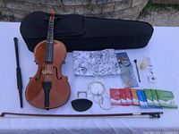 Full shot showing violin with bow, black case, recorder, shoulder rest, rosin, cleaning cloth, multiple sets of strings spread out on a white surface