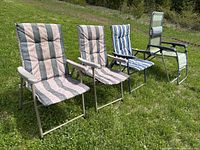 Four outdoor chairs set on grass including three folding lawn chairs with striped cushions and one green zero-gravity chair for lounging.