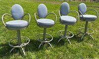 Four gray metal and blue fabric swivel bar stools placed outdoors on grass, showing full front and side views.