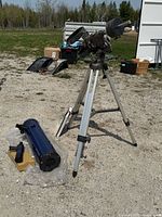 Sky Scan 2001 telescope optical tube and finder scope on ground, aluminum tripod mounted and standing behind outside on gravel surface.