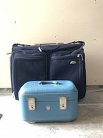 Front view of Samsonite suitcase behind smaller blue vanity travel bag, showing front pockets and handle.