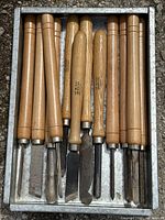 Top view of set of 14 woodworking tools in a metal tray with wooden handles and high speed steel blades showing wear.
