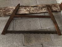 Full view of the antique bow saw showing its wooden frame and metal blade with rust.