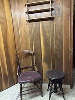 Antique wooden chair with curved backrest and worn red upholstered seat next to a round wooden stool with spindle legs.