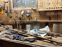 Workbench with various hand tools including saws, clamps, hammers, chisels, wrenches, screwdrivers, and a circular saw blade mounted on the back board. Tools show rust and wear.