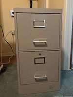 Front view of two-drawer beige metal filing cabinet showing wear and scratches.