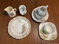 Overview of china tea plates arranged in stack showing different floral patterns. Set includes 3 plates, 2 creamers, and 2 teacup with saucers with distinct designs.