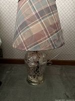 Full view of the lamp showing the plaid lampshade and the clear cut glass base sitting on a silver-tone platform.