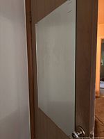 Frameless rectangular mirror mounted on door with clips visible, reflective surface clear but some marks might be present.