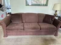 Front view of large brown fabric couch showing three seat cushions and three back cushions with two additional throw pillows on the ends.