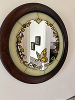 Front view of the vintage wall mirror showing the butterfly and floral stained glass design surrounding the round mirror center within a wooden frame.