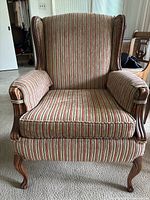 Front view of the traditional upholstered armchair showing the striped fabric in red, green, and beige. Wooden curved cabriole legs and padded armrests visible.