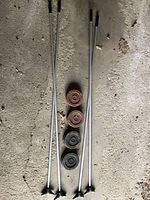 Full view of four metal shuffleboard tangs (two longer, two shorter) and four wooden discs (two brown, two black) aligned vertically on a concrete floor.