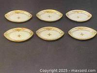 Six oval antique porcelain nuts dishes arranged in two rows on black cloth, showing consistent floral hand-painted design and gold rims.