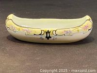 Side view of antique Nippon floral ceramic bowl shaped like a canoe. Shows hand painted yellow border with pink and purple flower details and dark accent at center.