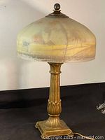 Full lamp upright on black surface showing brass base and painted glass shade