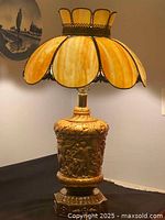 Full view of the amber slag glass lamp showing the ornate brass/plated base and scalloped multi-panel shade.