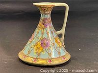 Front angle show of the ewer highlighting the body, handle, and intricate raised gold Moriage decoration with floral design on light blue background.
