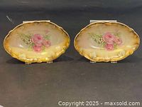 Two oval Baviaria dishes with pink roses and gold rims on display stands on a black surface