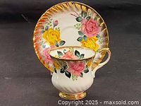 View of teacup on saucer showing pink and yellow roses with green leaves and gold trim on edges