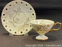 Front view of white porcelain teacup with gold floral pattern and matching saucer with lattice design.