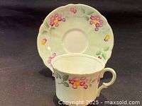 Photo showing front view of teacup with hand painted pink and yellow roses and green leaves, matching saucer with scalloped edge and floral decoration.