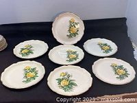 Six off-white ceramic sandwich plates with scalloped gold-trimmed edges and yellow rose design on each, displayed flat in a circular arrangement.