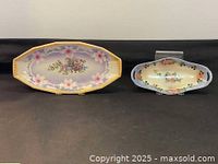 Two German hand painted oval dishes of different sizes, placed side by side against a black background