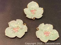 Set of three porcelain leaf-shaped trinket dishes with floral design and gold trim shown from above on black cloth.