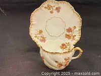 Teacup and saucer viewed from above showing floral decoration and scalloped edges with gold trim