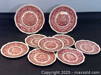 All nine plates arranged on a table, showing two larger dinner plates and seven smaller side plates with pink transferware design.