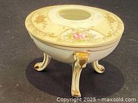 Side view of the porcelain Nippon hair receiver showing the three gold-painted legs and floral design.