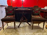 Front view of pair of Victorian walnut chairs with floral needlepoint upholstery and detailed wood carvings, alongside a folding table.