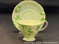 Teacup and saucer set shown together on black background, highlighting the snowdrops pattern and pale green color.