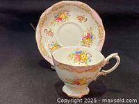 Full view of teacup and saucer showing pink floral hand painted pattern with gold trim.