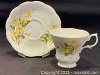 Royal Albert Primrose floral hand painted teacup and saucer displayed separately, showing yellow primrose flowers, gold trim on edges, and scalloped porcelain design.