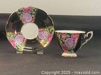 Photo showing a Royal Standard fine china teacup and matching saucer with pink rose and hydrangea floral pattern on a black background accented with gold trim. The cup height is about 2.75 inches and the saucer is 5.75 inches in diameter.