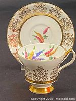 Photo showing the cup and saucer from the front, highlighting the intricate gold filigree and multicolor wheat design patterns.