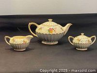 Full view of tea set including teapot, creamer, and sugar bowl on black surface