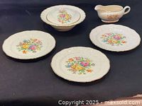 Full view of all pieces: three dinner plates, covered tureen, gravy boat, all decorated with floral needlepoint designs and gold trim.
