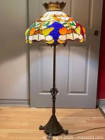 Full view of the Tiffany style floor lamp showing stained glass fruit pattern shade and brass finish base.